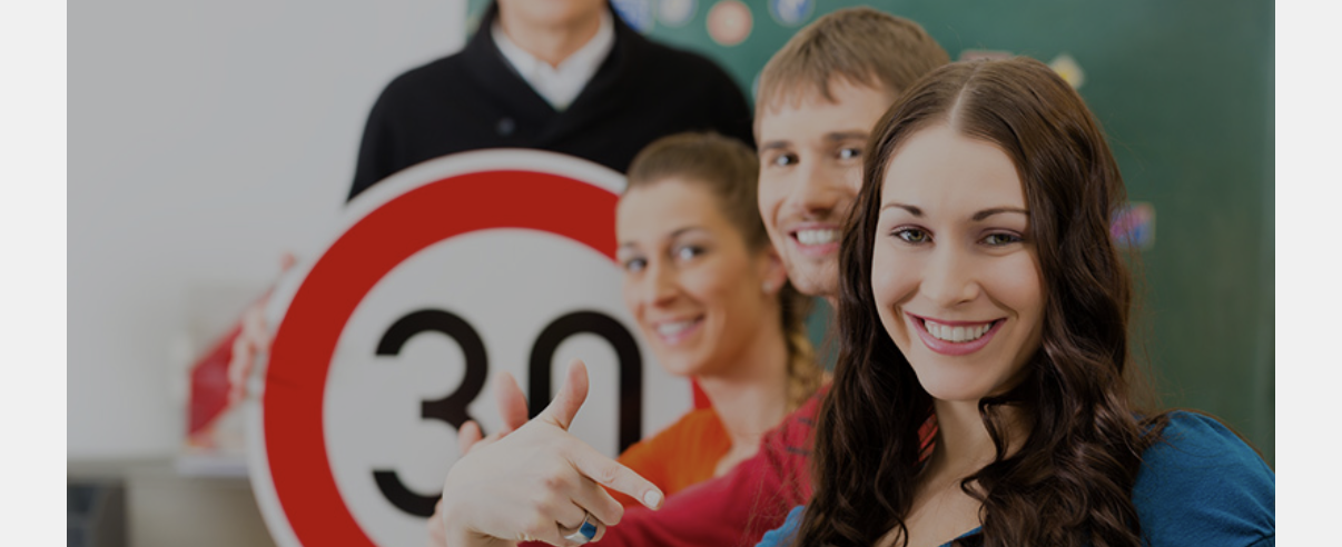 Gruppe junger Erwachsener mit Tempo-30-Schild im Fahrschulunterricht